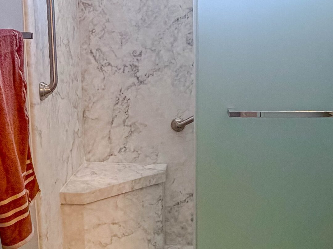Walk-in shower with marble-look walls, a built-in bench and a grab bar