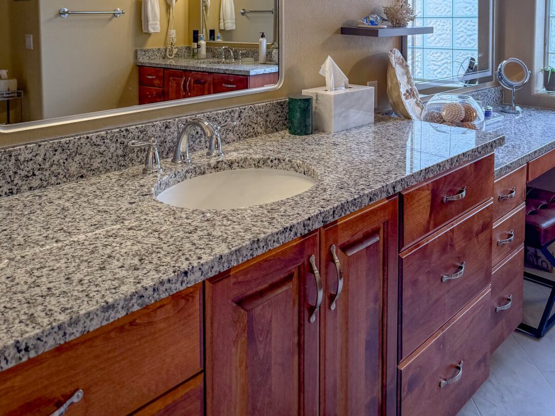 Long bathroom vanity with a stone top, cherry cabinets and a full framed mirror