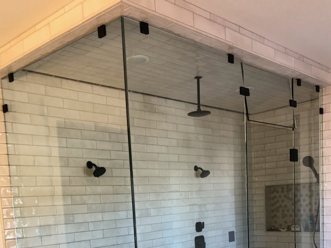 Walk-in frameless glass shower with dual rain heads and pebble tile flooring
