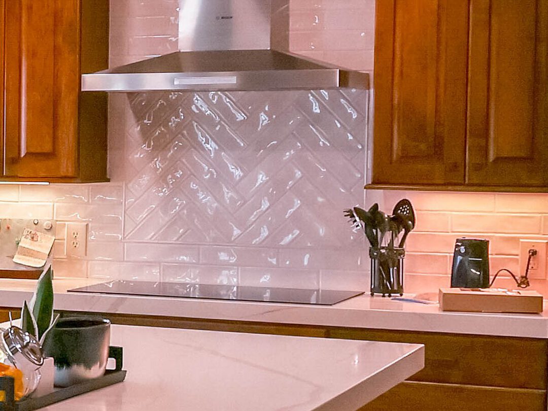 Herringbone tile backsplash behind a cooktop under a stainless vent hood
