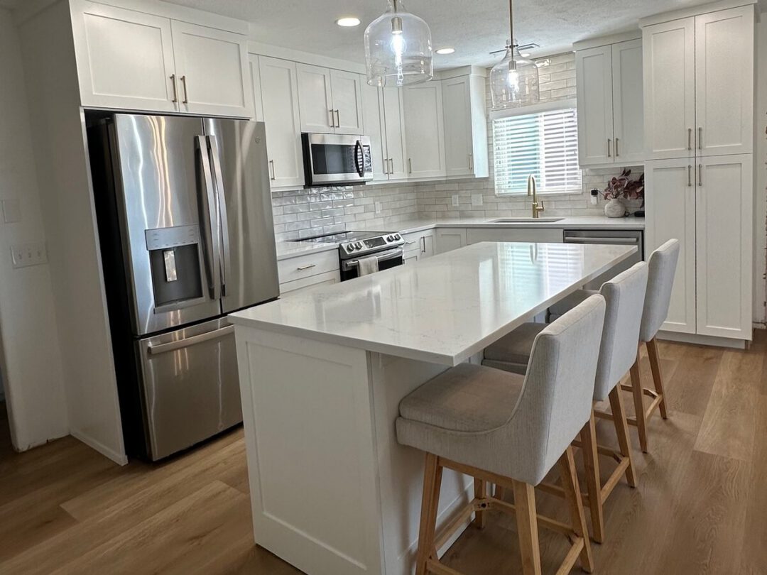 White shaker kitchen with a quartz island, glass pendants and stainless appliances