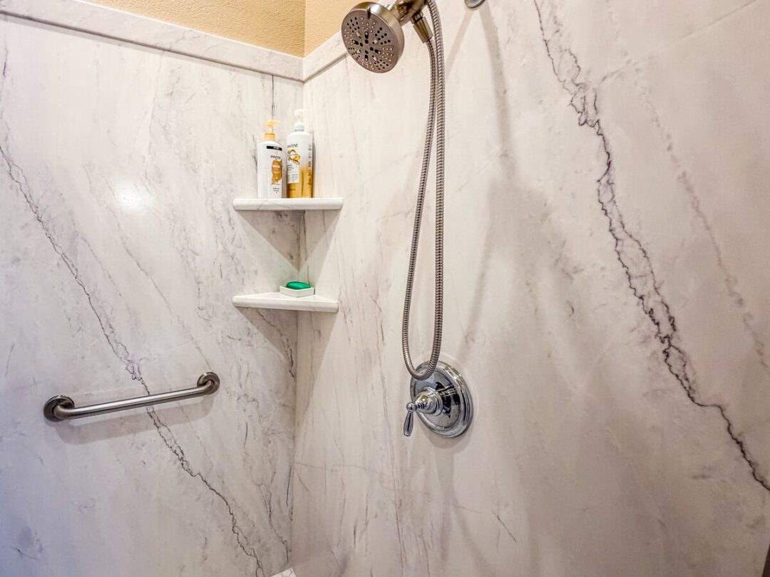 Walk-in shower with solid-surface walls, a grab bar and a sliding handheld sprayer
